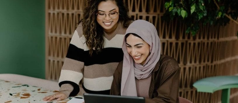 Students smiling and looking at college programs on a laptop computer.