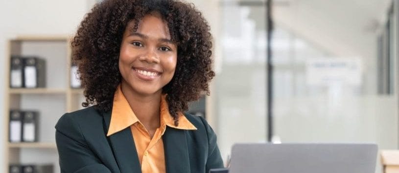 Woman in a blazer smiling while at a laptop. Take Business and Law programs at CCHST.